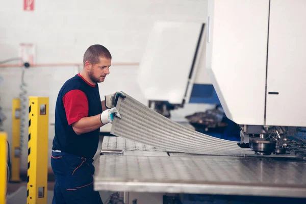 Dentro de una fábrica, trabajador industrial en acción en la máquina de la prensa del metal que sostiene un pedazo de acero listo para ser trabajado . — Foto de Stock