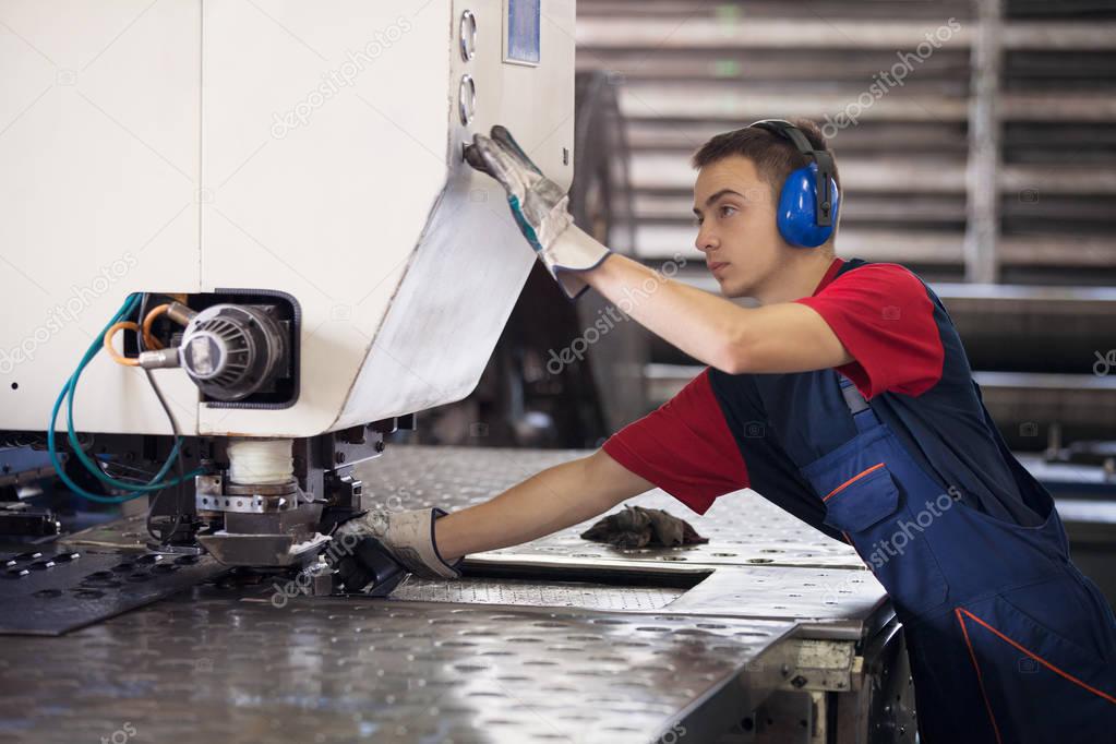 Inside a factory, industrial worker in action on metal press machine holding a steel piece ready to be worked.