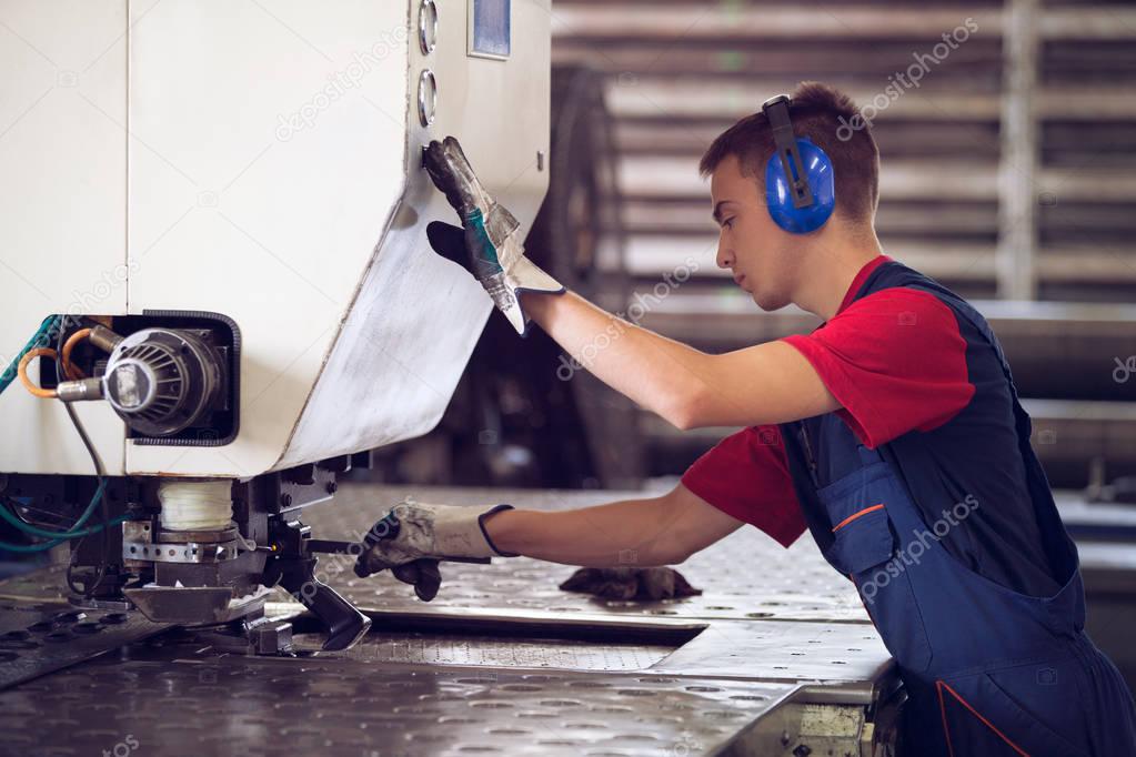 Inside a factory, industrial worker in action on metal press machine holding a steel piece ready to be worked.