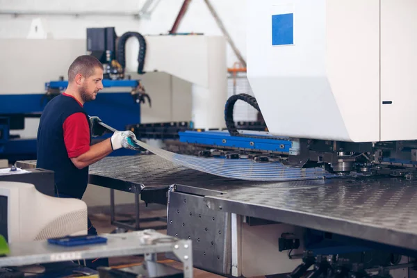 Dentro de una fábrica, trabajador industrial en acción en la máquina de la prensa del metal que sostiene un pedazo de acero listo para ser trabajado . — Foto de Stock