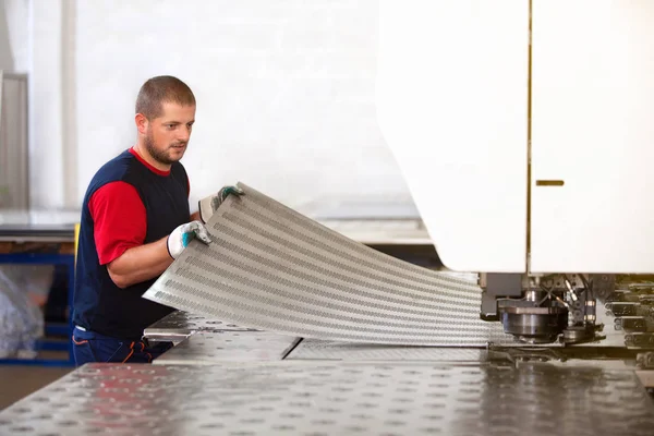 Dentro de una fábrica, trabajador industrial en acción en la máquina de la prensa del metal que sostiene un pedazo de acero listo para ser trabajado . — Foto de Stock