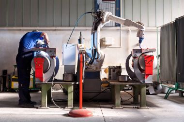 İşçi metal parçalar robotized kolu ile kaynak için hazırlar.