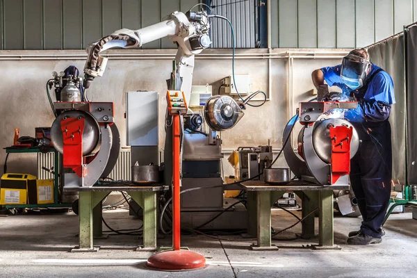 İşçi metal parçalar robotized kolu ile kaynak için hazırlar.