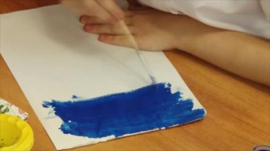 Çocuk bir fırça ve kağıt üzerine guaj boyalar