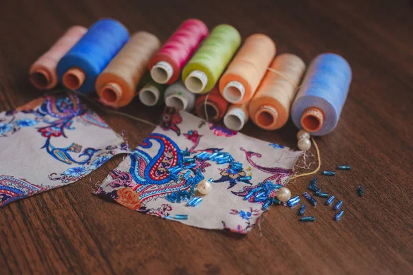 fabric pieces with bead and colorful thread on the wooden table