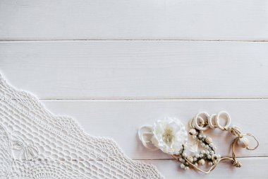 A piece of crocheted light tablecloth and flower costume jewelry on a white wooden background. Vintage background with space for text clipart