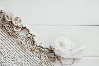 Beyaz ahşap arka planda örülmüş bir masa örtüsü ve çiçek kostümlü mücevher. Metin için alanı olan eski arkaplan