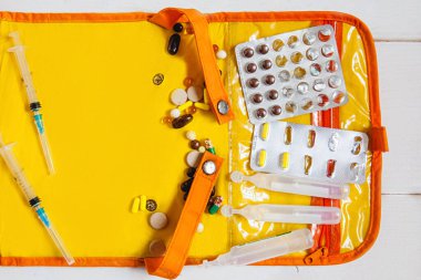 Turuncu bir ilk yardım çantasının arka planına renkli tabletler, ampuller ve şırıngalar serpiştirilmiş. Mesaj için yer var. Virüs saldırısı konsepti.