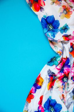 Parlak mavi arka planda kumaşlı, çok renkli çiçekleri olan beyaz bir kumaş parçası. Mesaj için yer var. Tasarım konsepti