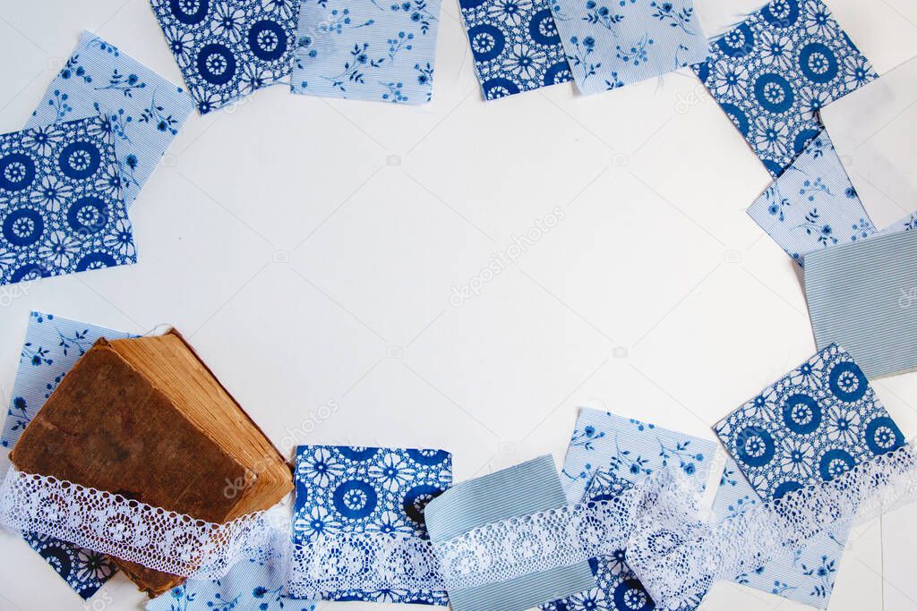 Square patches of blue printed fabric, old shebby book and white lace on a white background. Textile frame with space for text