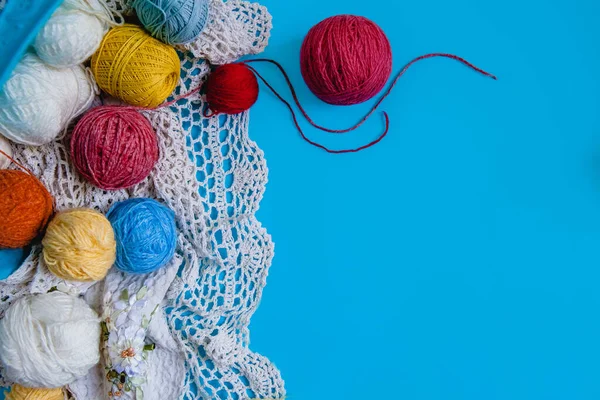 Scattered colored balls of thread and a white knitted tablecloth on a blue background. Flat layout with space for text