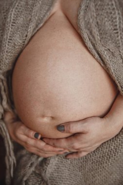 Örgü örmüş hamile bir kadın karnını tutuyor. Hamilelik dönemi uzadı. Karnı yakın.