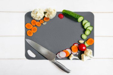 Gri kesim tahtası, çeşitli sebzeler ve beyaz ahşap bir arka planda aşçı bıçağı. Düz Düzen.