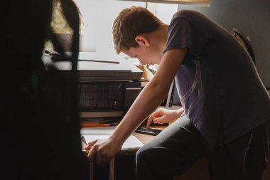 Evde kıyafetlerini giymiş genç bir çocuk bir masaya oturur ve akıllı telefon kullanarak ders alır. Uzaktan eğitim