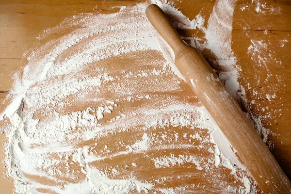 Spilled flour and a wooden rolling pin on a wooden table. The view from the top