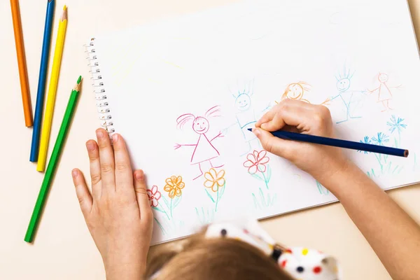 Little child draws a family with pencils, top view