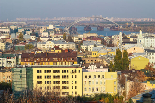 A panoramic city view on Kyiv from a hill. In the middle, there is a Dnieper river and a bridge joining two shores of the river