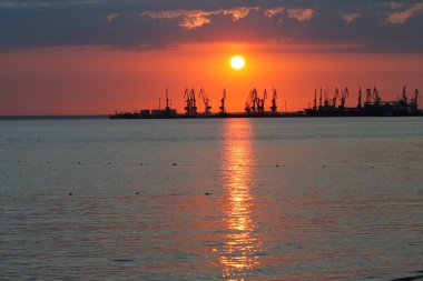 Ateşli günbatımı gökyüzü ve deniz ile güzel bir manzara. Gün doğarken kıyıda liman. Turna siluetleri ateşli, turuncu ve kırmızı gökyüzüne karşı.