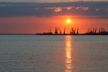 Ateşli günbatımı gökyüzü ve deniz ile güzel bir manzara. Gün doğarken kıyıda liman. Turna siluetleri ateşli, turuncu ve kırmızı gökyüzüne karşı.