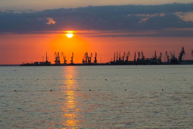 Ateşli günbatımı gökyüzü ve deniz ile güzel bir manzara. Gün doğarken kıyıda liman. Turna siluetleri ateşli, turuncu ve kırmızı gökyüzüne karşı.