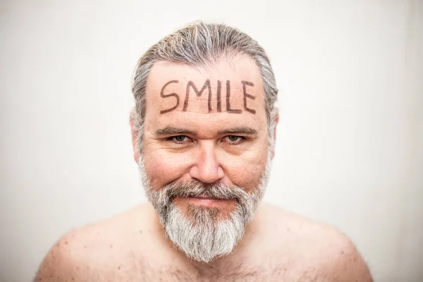 Portrait of a shirtless man with the word smile written on the forehead