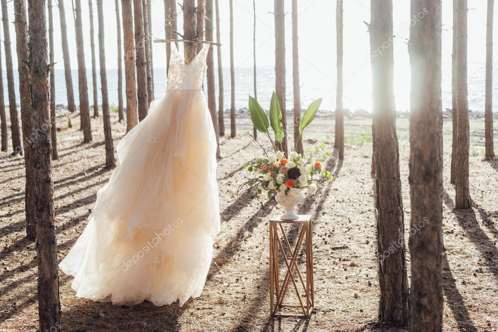 close-up photo of beautiful wedding dress near bouquet of spring flowers on forest background