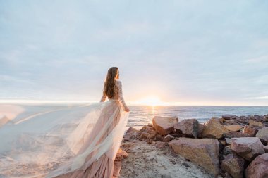 genç güzel kadın gelinlikle deniz kıyısında günbatımı poz 