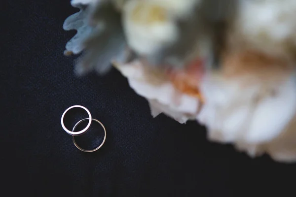 ウェディング ブーケと黒い背景にダイヤモンドの 2 つの金の結婚指輪 — ストック写真