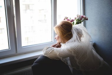 Güzel bir gülümseme ile gelin dışarı bekleyen damat penceresinde görünüyor. Gelin bir güzel saç ve makyaj