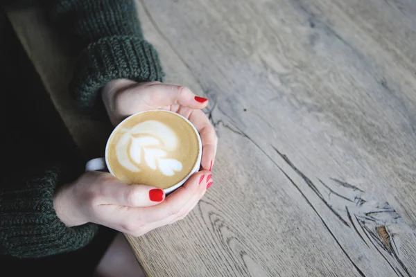 Женская рука держать чашку кофе с сердцем формы на деревянный стол — стоковое фото