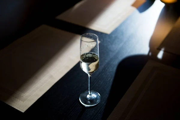 Una copa de champán cagada en una mesa de madera oscura al atardecer — Foto de Stock