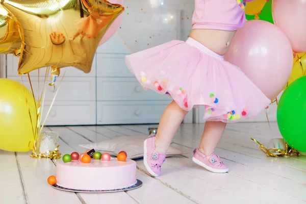 Klein meisje in een roze pluizige rok. Roze mousse taart met kleurrijke ballen op een witte houten vloer — Stockfoto