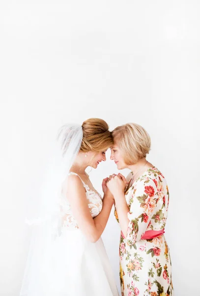 Manhã de casamento da noiva. Mãe da noiva abençoa a noiva para uma vida familiar feliz. A mãe e a filha deram as mãos. No fundo uma parede brilhante — Fotografia de Stock