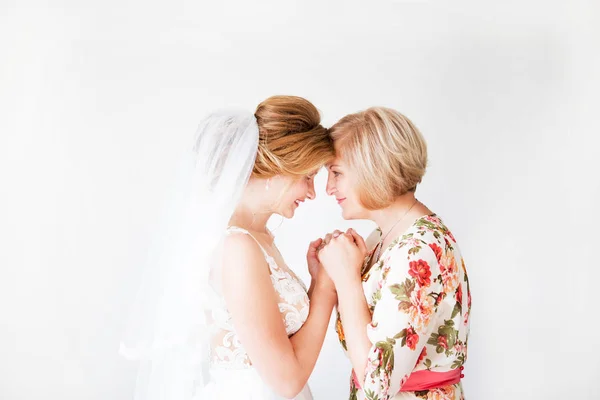 Manhã de casamento da noiva. Mãe da noiva abençoa a noiva para uma vida familiar feliz. A mãe e a filha deram as mãos. No fundo uma parede brilhante — Fotografia de Stock