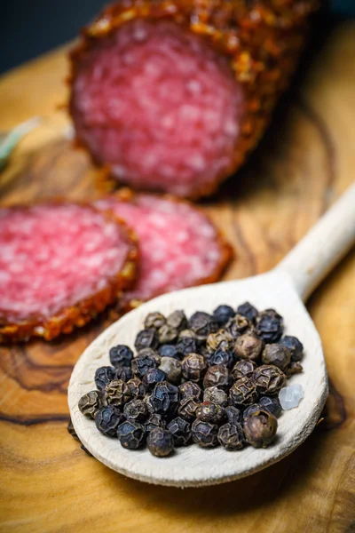 Salami seco con costra en pimienta roja molida sobre fondo oscuro — Foto de Stock