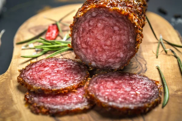 Salami seco con costra en pimienta roja molida sobre fondo oscuro — Foto de Stock