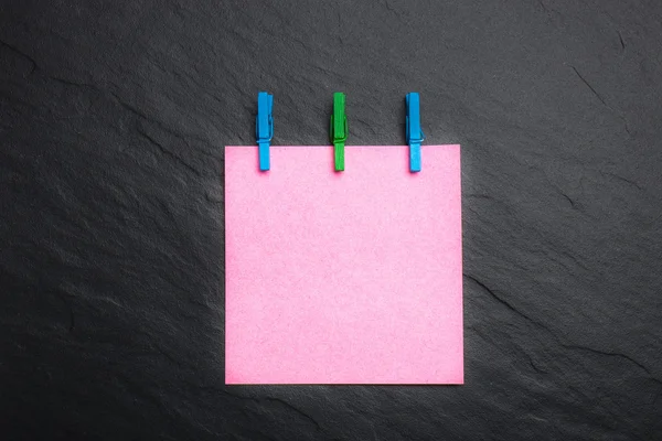 Nahaufnahme eines rosafarbenen Notenpapiers und Wäscheklammern auf schwarzem Hintergrund — Stockfoto
