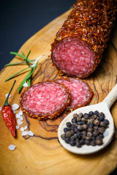 Salami seco con costra en pimienta roja molida sobre fondo oscuro — Foto de Stock