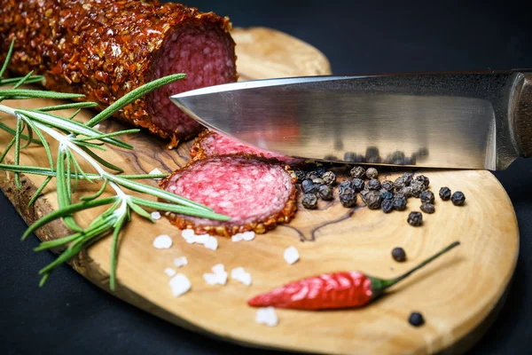 Salami seco con costra en pimienta roja molida sobre fondo oscuro — Foto de Stock