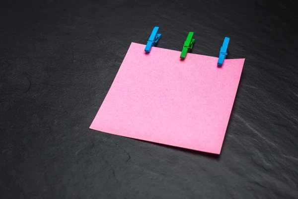 Close up of a pink note paper and clothes pegs on a black background — Stock Photo, Image