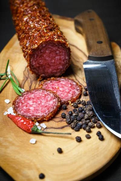 Salame seco crostado em pimenta vermelha moída em fundo escuro — Fotografia de Stock