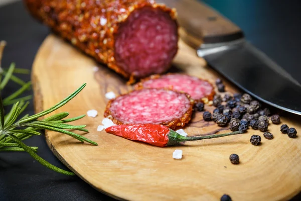 Salame seco crostado em pimenta vermelha moída em fundo escuro — Fotografia de Stock