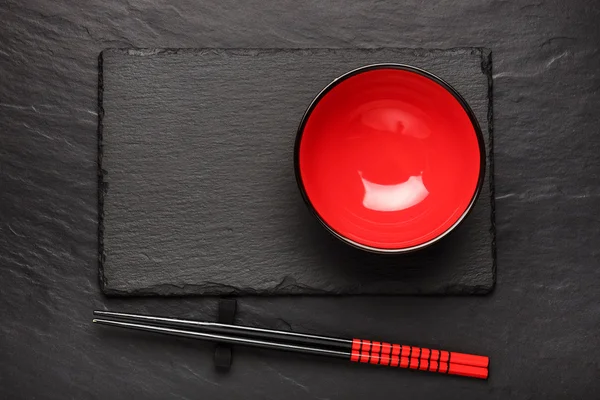 Two chopsticks and red plate on black stone background with copyspace, top view — Stock Photo, Image