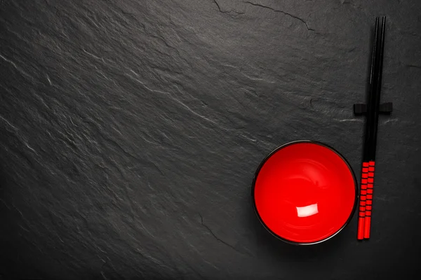 Two chopsticks and red plate on black stone background with copyspace, top view — Stock Photo, Image