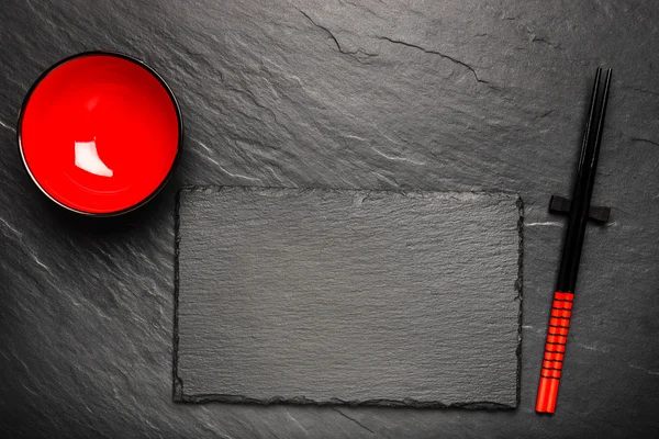 Kaksi syömäpuikkoa ja punainen levy musta kivi tausta copyspace, ylhäältä — kuvapankkivalokuva