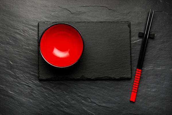 Two chopsticks and red plate on black stone background with copyspace, top view — Stock Photo, Image