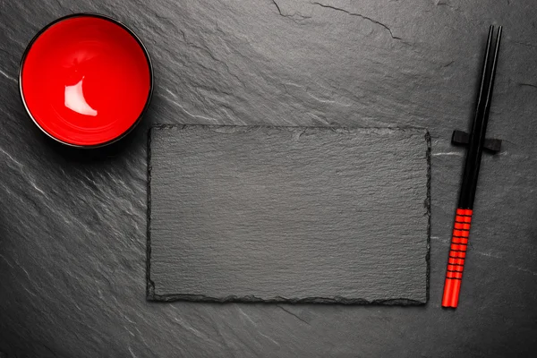 Zwei Essstäbchen und roter Teller auf schwarzem Steinhintergrund mit Kopierraum, Draufsicht — Stockfoto