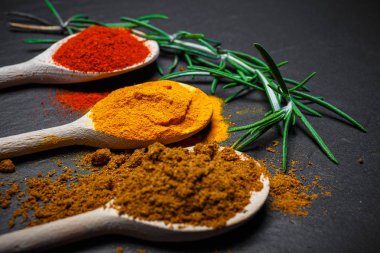 tahta kaşıklar üzerinde siyah taş zemin, üstten görünüm içinde baharatlar