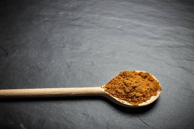 tahta kaşıklar üzerinde siyah taş zemin, üstten görünüm içinde baharatlar