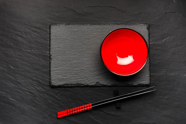 Two chopsticks and red plate on black stone background with copyspace, top view — Stock Photo, Image